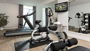 Un gimnasio en casa con cinta de correr, elíptica y bicicleta estática, un espejo grande y un televisor en la pared.