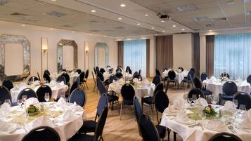 Ein Bankettsaal mit runden Tischen, gedeckt für ein Essen, mit weißen Tischdecken und blauen Stühlen.