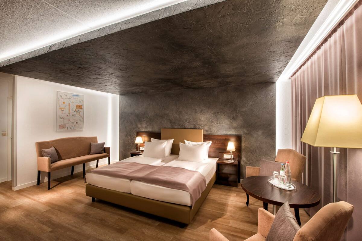 Une chambre d’hôtel moderne avec un grand lit, un canapé, une petite table avec une lampe et un tableau au mur.