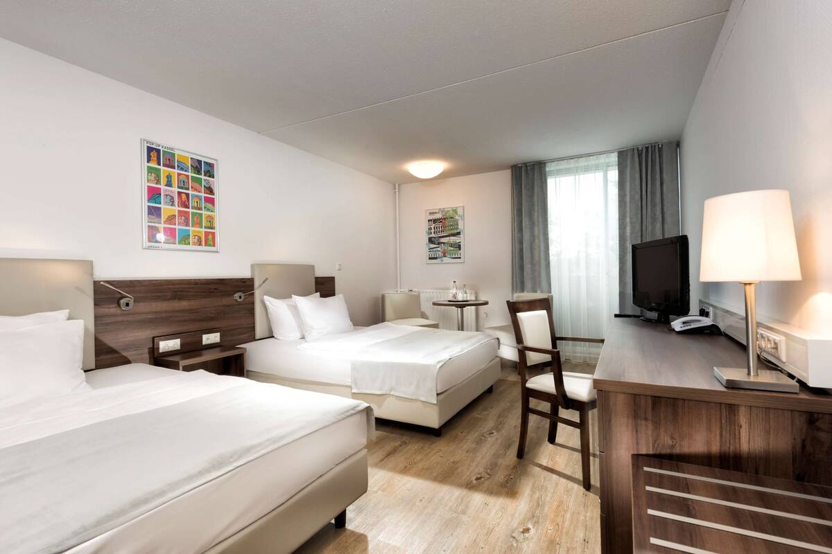 Une chambre d’hôtel avec deux lits, un bureau, une chaise, une télévision et une lampe.
