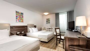 A hotel room with two beds, a desk, a chair, a TV, and a lamp.