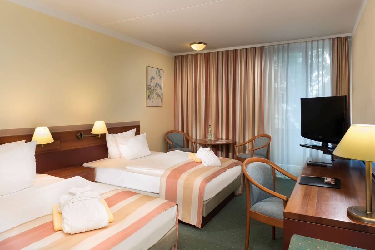 Une chambre d’hôtel avec deux lits, un bureau avec une télévision, une chaise et une table avec une lampe.