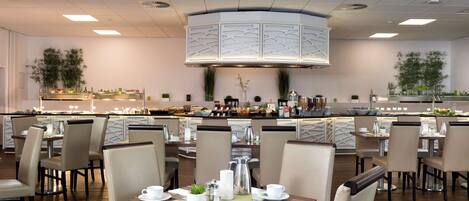 Un comedor moderno con varias mesas y sillas, una zona de bar central con techo decorativo y una cocina al fondo.