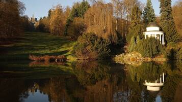 A tranquil garden with a reflective pond, a gazebo, and a distant building.