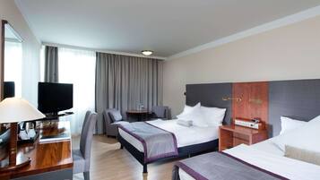 Habitación de hotel con dos camas, un escritorio con lámpara, televisión, una mesita y una silla.