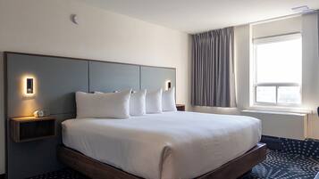 Una habitació d'hotel amb un llit gran, una taula de nit amb un rellotge, un capçal de llit amb il·luminació integrada, una finestra amb cortines i una catifa amb disseny.
