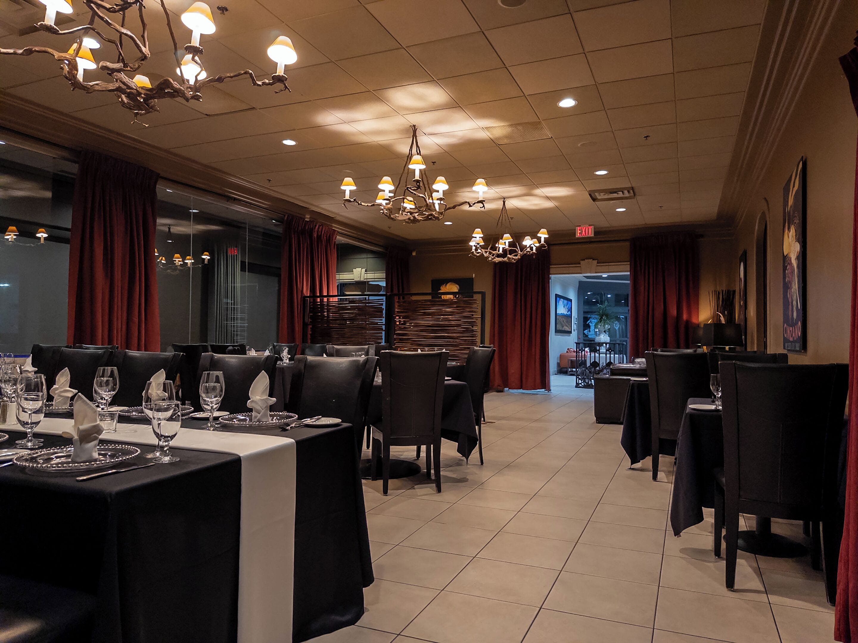 A restaurant with tables set for dining, a chandelier, and red curtains.