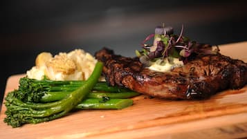 A steak with a garnish of greens and a side of mashed potatoes on a wooden board.