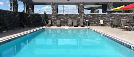 A swimming pool with stone walls and multiple lounge chairs.