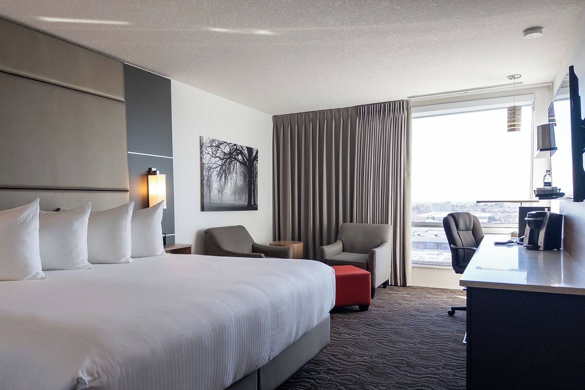 A hotel room with a large bed, two armchairs, a desk, and a view of the city.