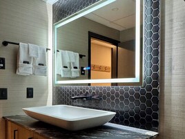 Un baño moderno con un espejo grande, un lavabo blanco tipo recipiente y un perchero con toallas blancas.