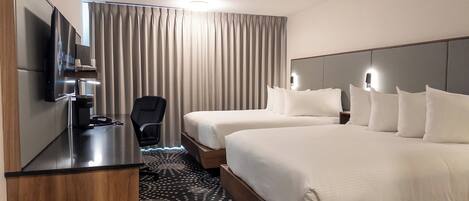 A hotel room with two beds, a desk with a flat-screen TV, a chair, and a large window with curtains.
