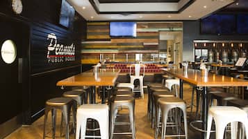 Una zona de bar con taburetes, una barra larga y un televisor montado en la pared.