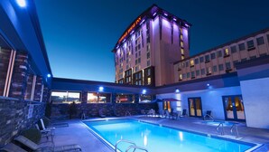 A hotel with a swimming pool, outdoor seating, and a view of the cityscape at dusk. - Carriage House Hotel & Conference Centre (Calgary)