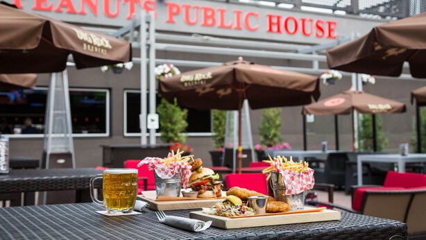 An outdoor dining area with tables, umbrellas, and a menu of food items. - Carriage House Hotel & Conference Centre (Calgary)