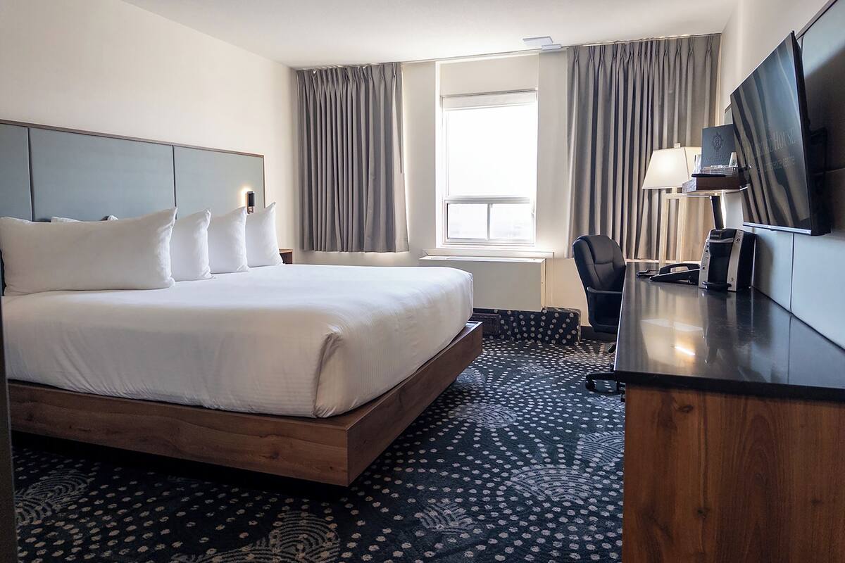 A hotel room with a large bed, a desk with a chair, a flat-screen TV, and a window with curtains.