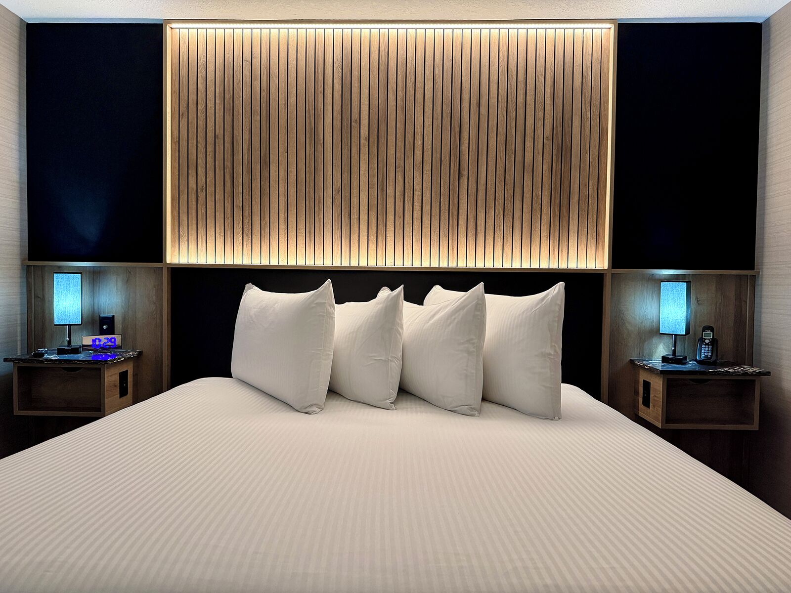 A modern hotel room with a large bed, a wooden headboard, and bedside tables with lamps.