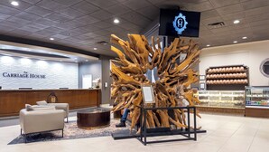 A reception area with a wooden sculpture centerpiece, a reception desk, and a bakery display. - Carriage House Hotel & Conference Centre (Calgary)