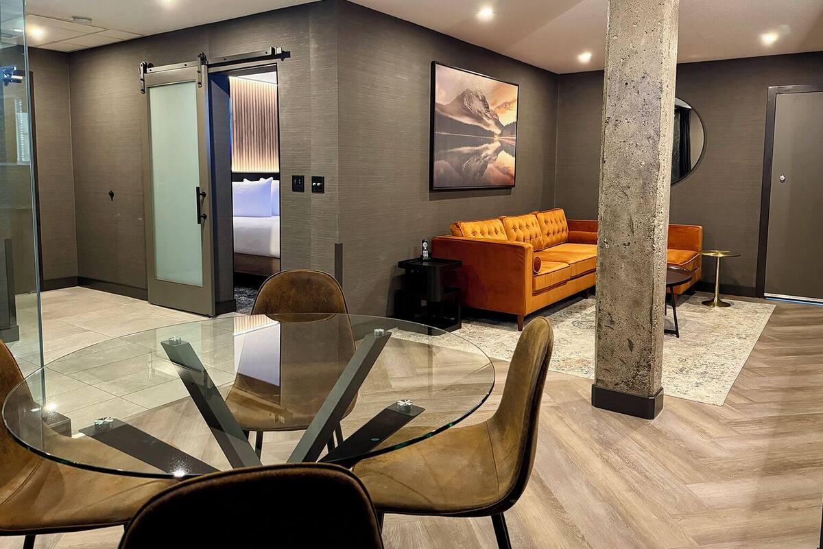 A modern hotel room with a glass dining table, a sofa, and a bed with a sliding door.