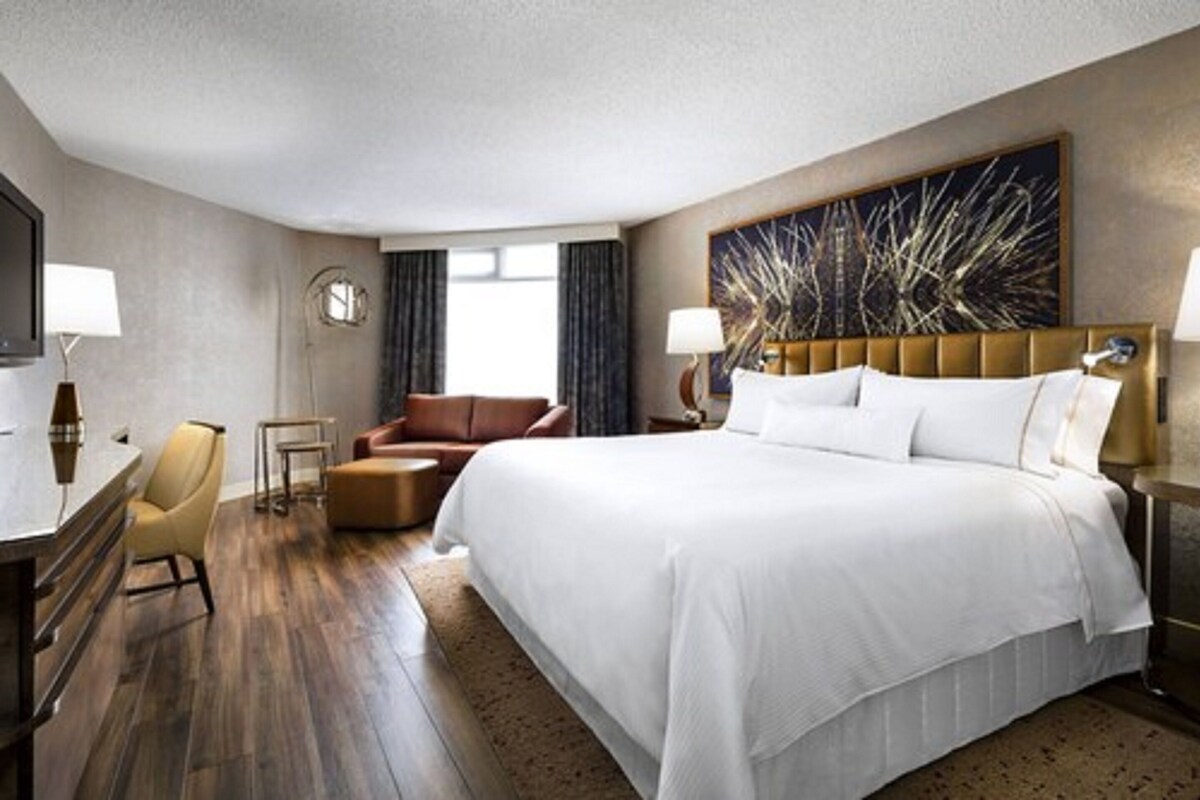 A hotel room with a large bed, a desk with a chair, a sofa, and a large painting on the wall.