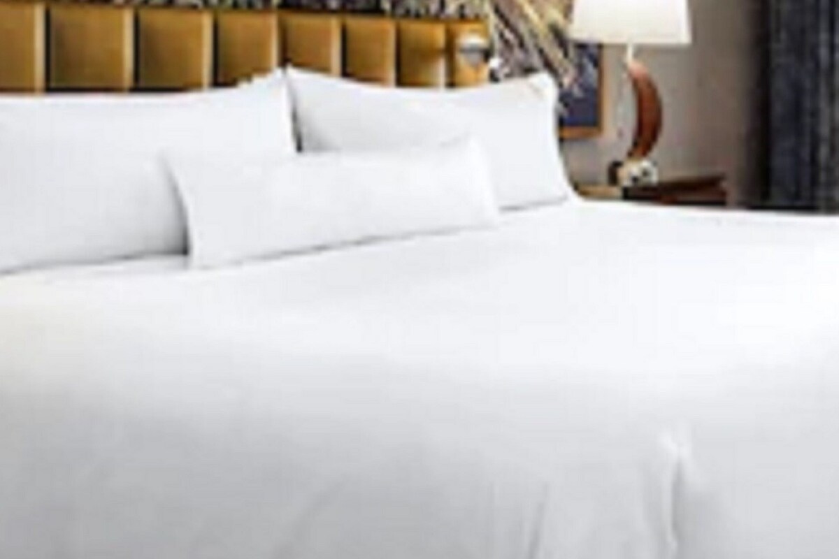 A neatly made bed with white linens and a wooden headboard.