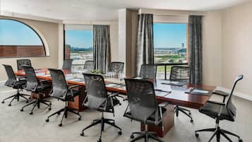 A conference room with a long table, multiple chairs, and large windows with curtains.