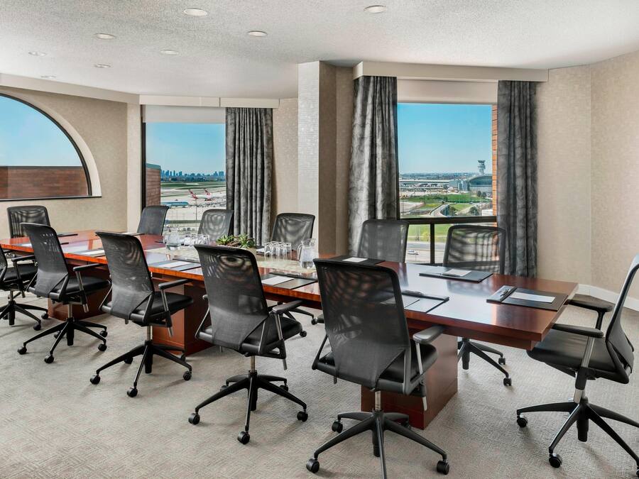 A conference room with a long table, multiple chairs, and large windows with curtains.