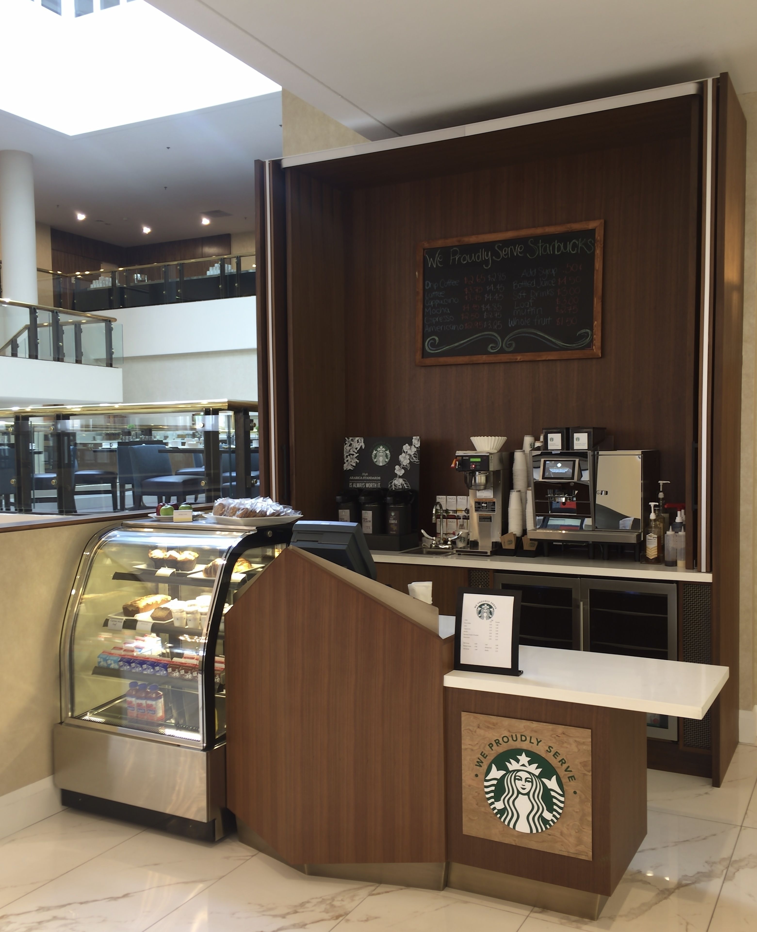 Una cafetería Starbucks con una vitrina de pasteles, una máquina de café y un menú en una pizarra.