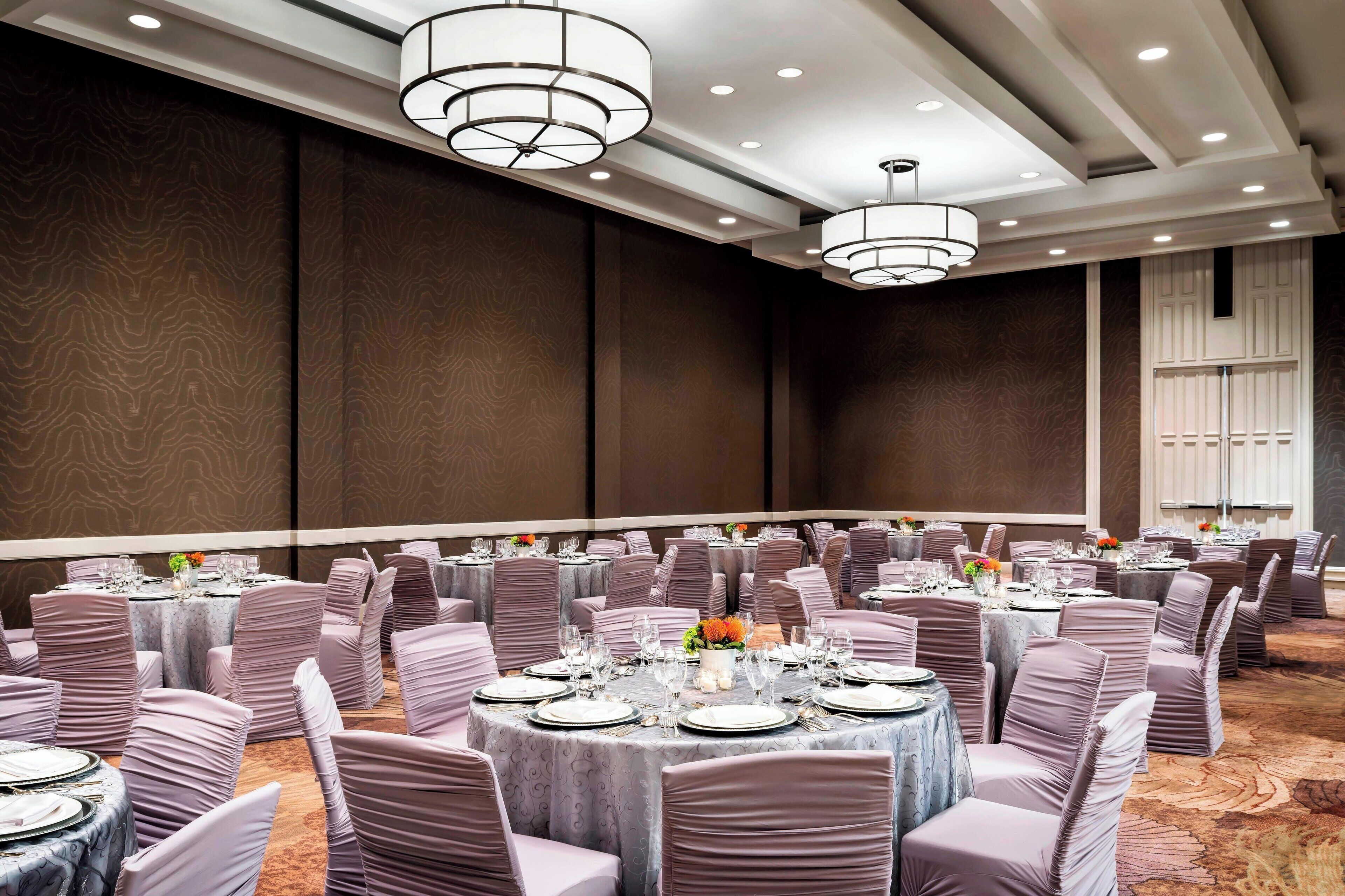 A banquet hall with round tables, chairs, and chandeliers.