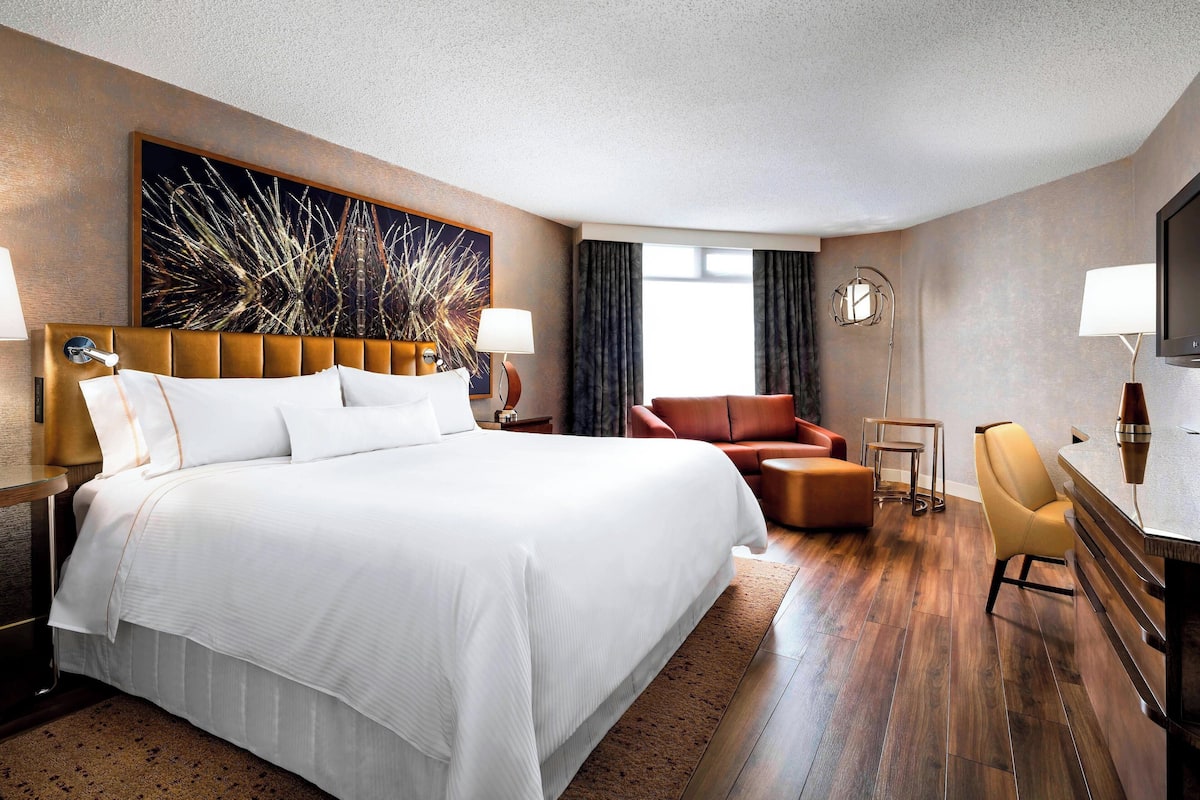 A hotel room with a large bed, a desk with a chair, a sofa, and a television.