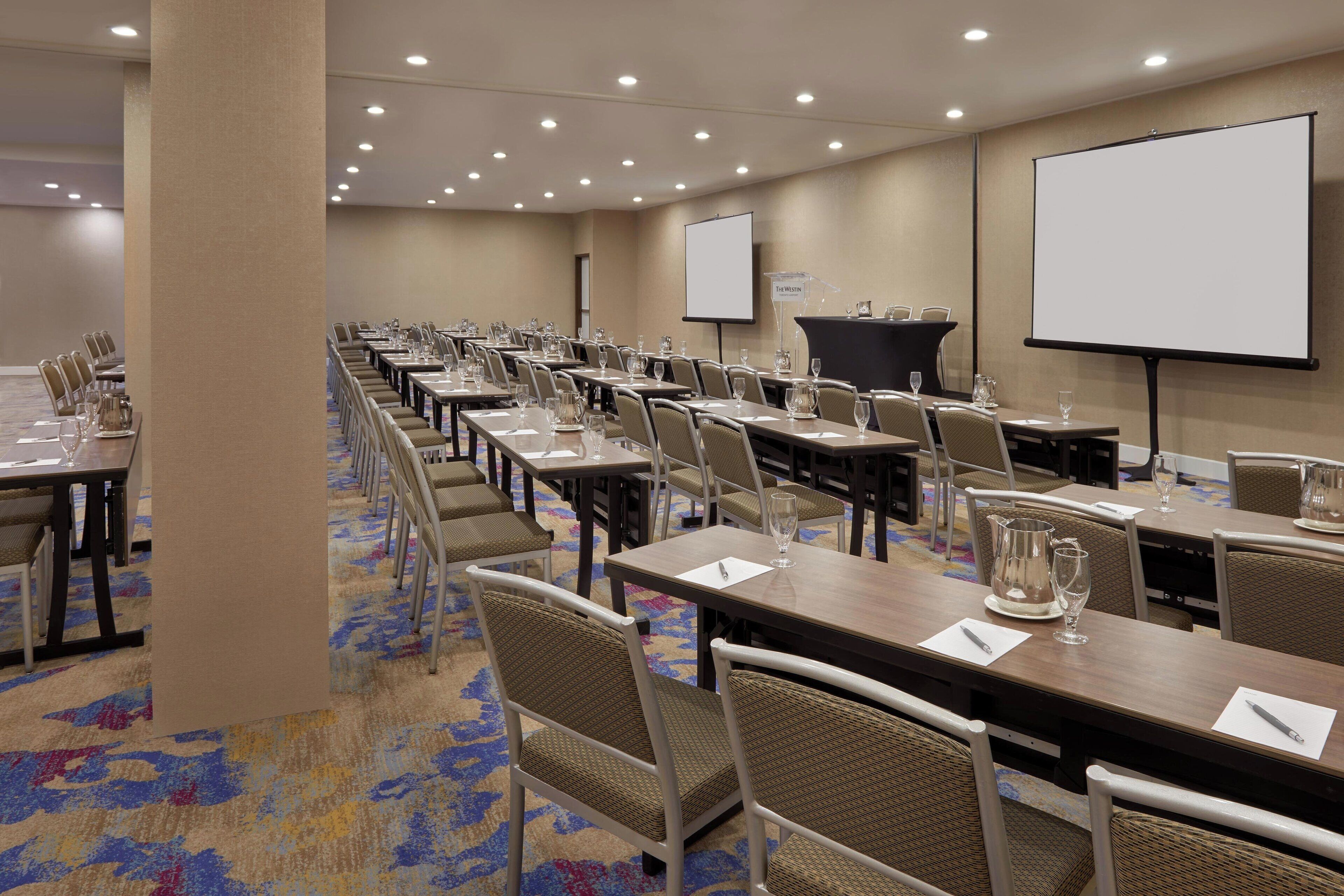 Una sala conferenze con file di tavoli, sedie e un grande schermo.