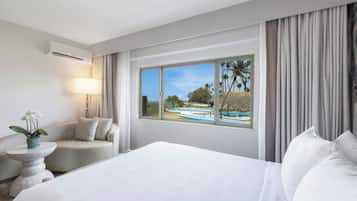 Une chambre d’hôtel avec un grand lit, un coin salon avec une lampe et une fenêtre donnant sur des bateaux et des palmiers.