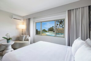 A hotel room with a large bed, a seating area with a lamp, and a window with a view of boats and palm trees. - Maui Seaside Hotel (Kahului)