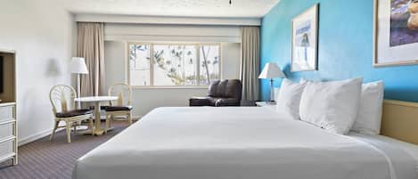 Habitación de hotel con una cama grande, un escritorio con silla, ventilador de techo y ventana con vista a palmeras.