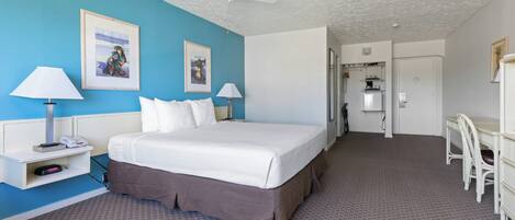 Quarto de hotel com uma cama, duas mesas de cabeceira com luminárias, um ventilador de teto e uma escrivaninha com cadeiras.
