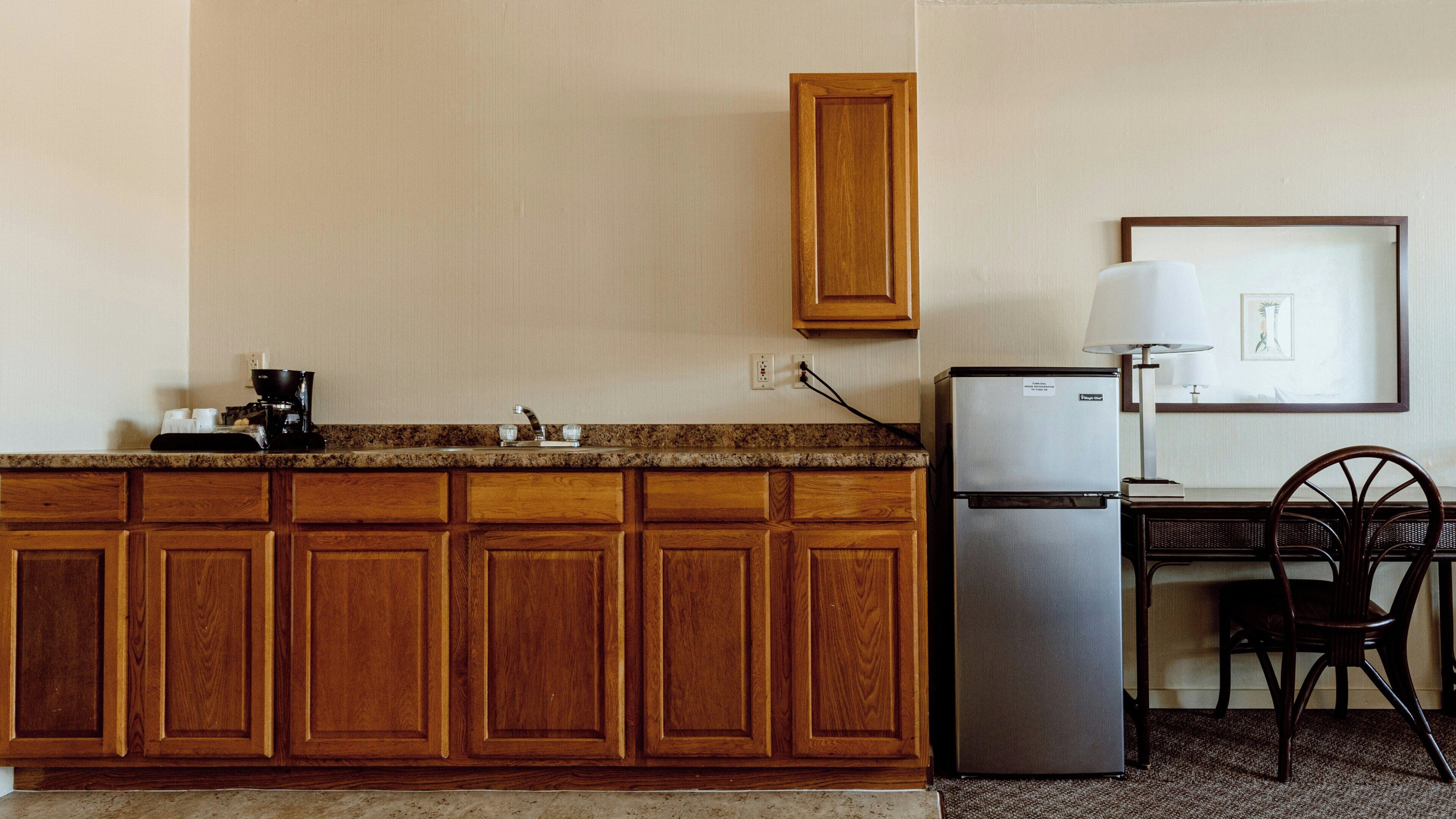 A kitchen with wooden cabinets, a refrigerator, a coffee maker, and a dining area with a chair and table.