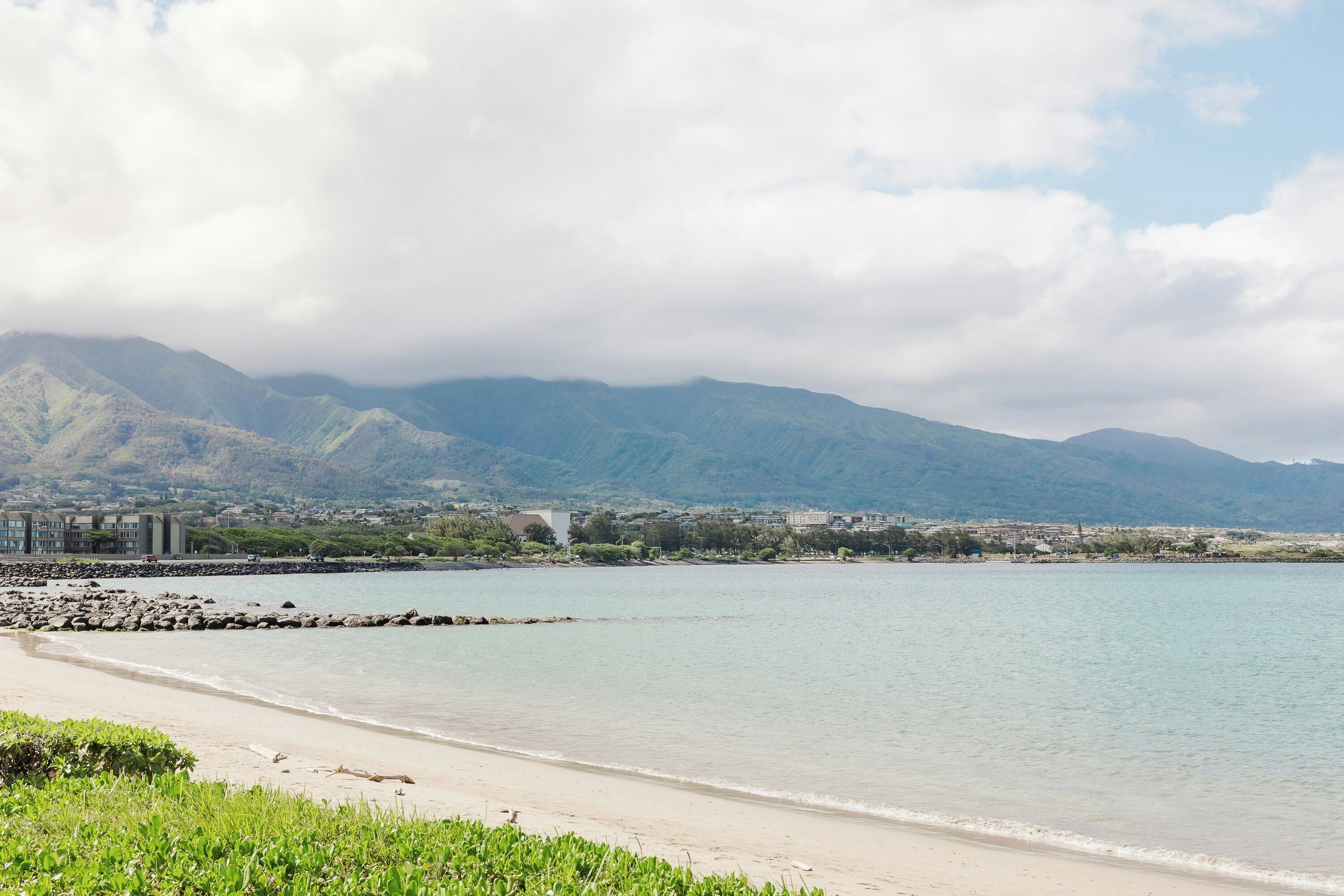 Ein Strand mit felsigem Ufer, ruhiger See und Bergen im Hintergrund.