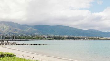 Ein Strand mit felsigem Ufer, ruhiger See und Bergen im Hintergrund.