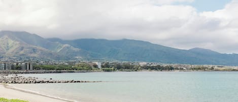 A beach with a rocky shoreline, a calm sea, and mountains in the background.