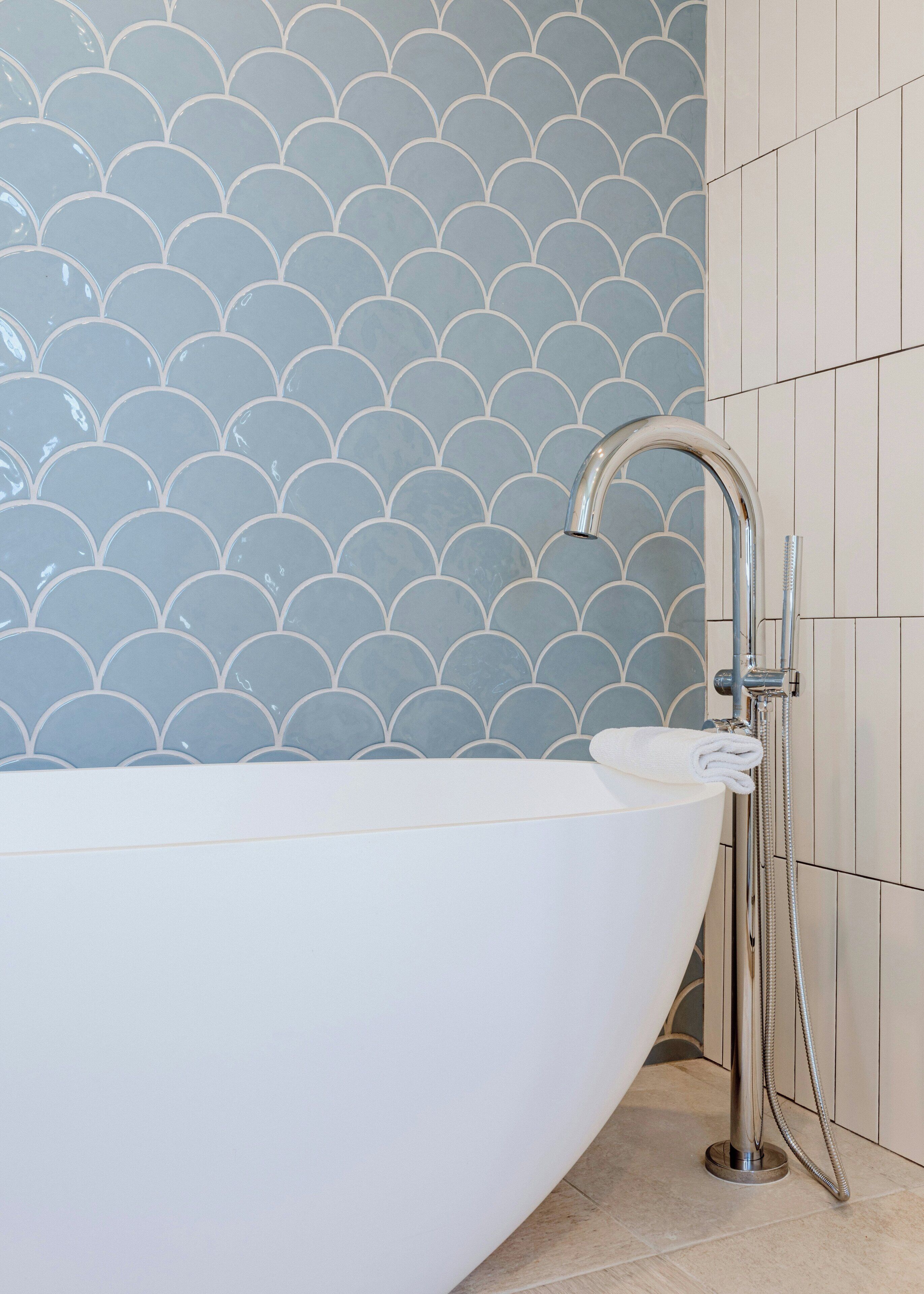 Een moderne badkamer met een vrijstaand bad, een douchekop en een betegelde muur met een getande rand.