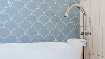 A modern bathroom with a freestanding bathtub, a showerhead, and a tiled wall with a scalloped pattern.