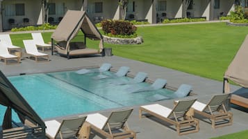 A pool area with lounge chairs, a small garden, and a building with multiple windows and balconies.