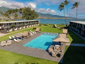 A resort pool area with lounge chairs, a swimming pool, and a view of the ocean and mountains. - Maui Seaside Hotel (Kahului)