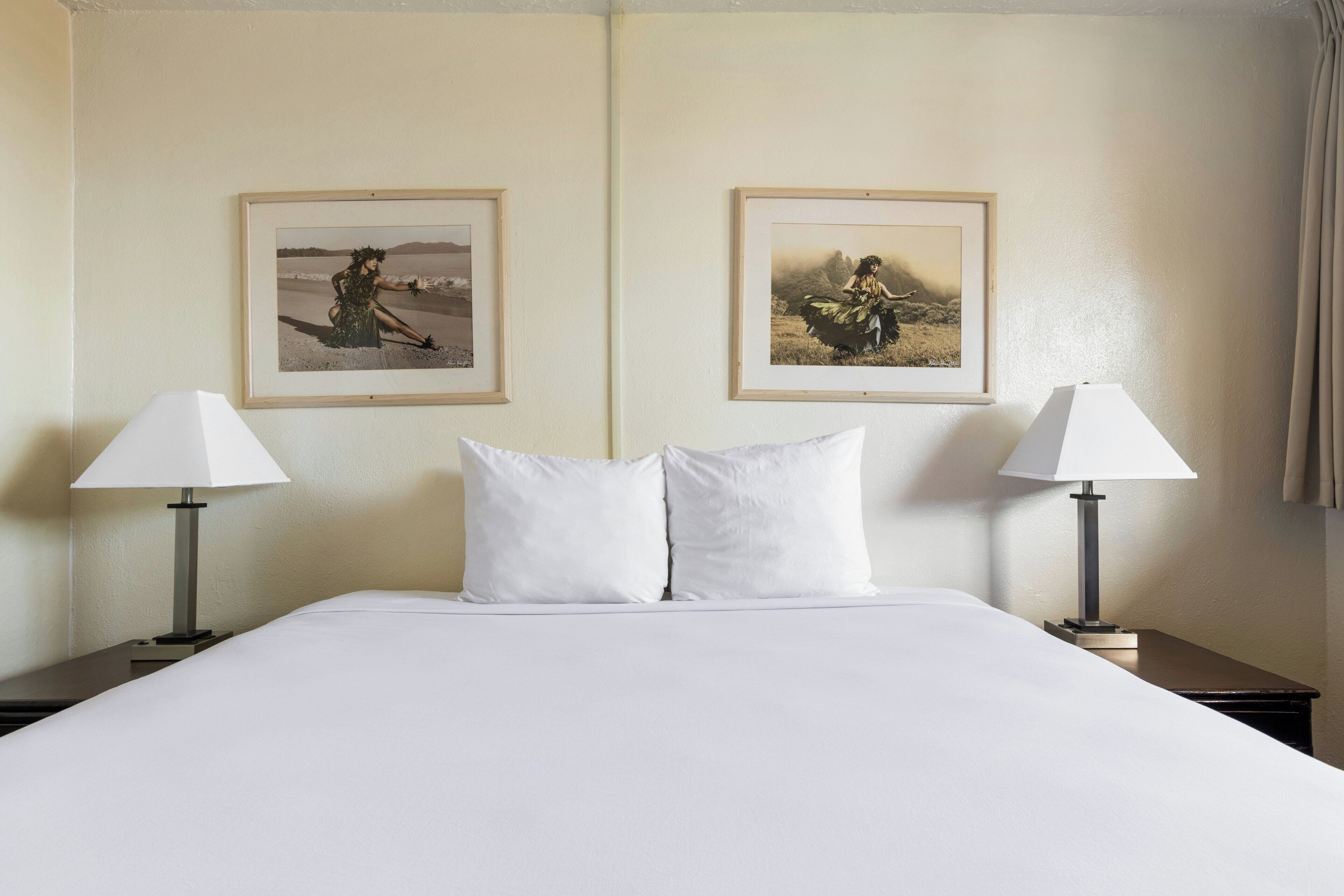 Une chambre d’hôtel avec un grand lit, deux lampes de chevet et deux tableaux encadrés au mur.