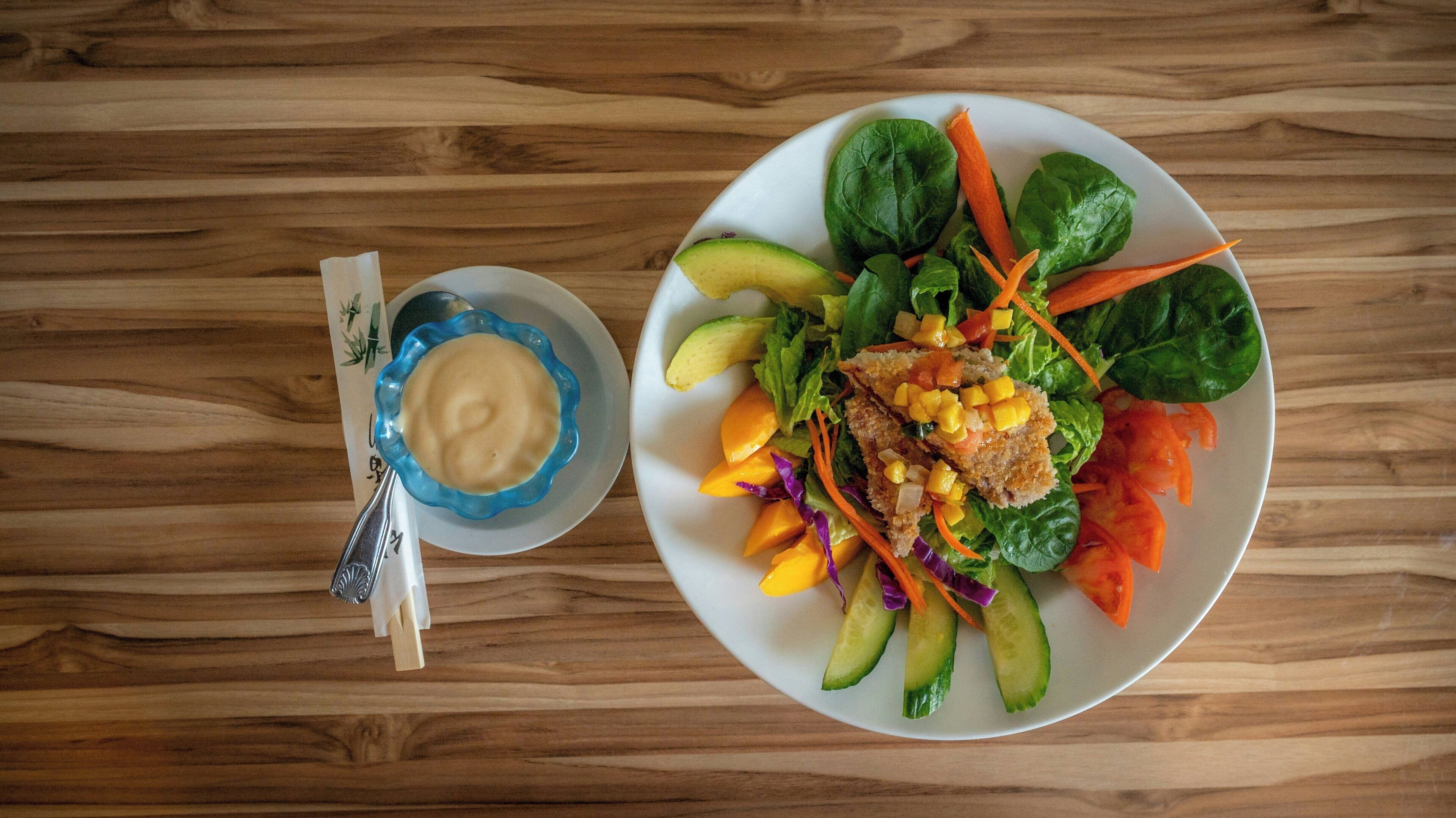 A plate of food with vegetables and a bowl of sauce on a wooden table.