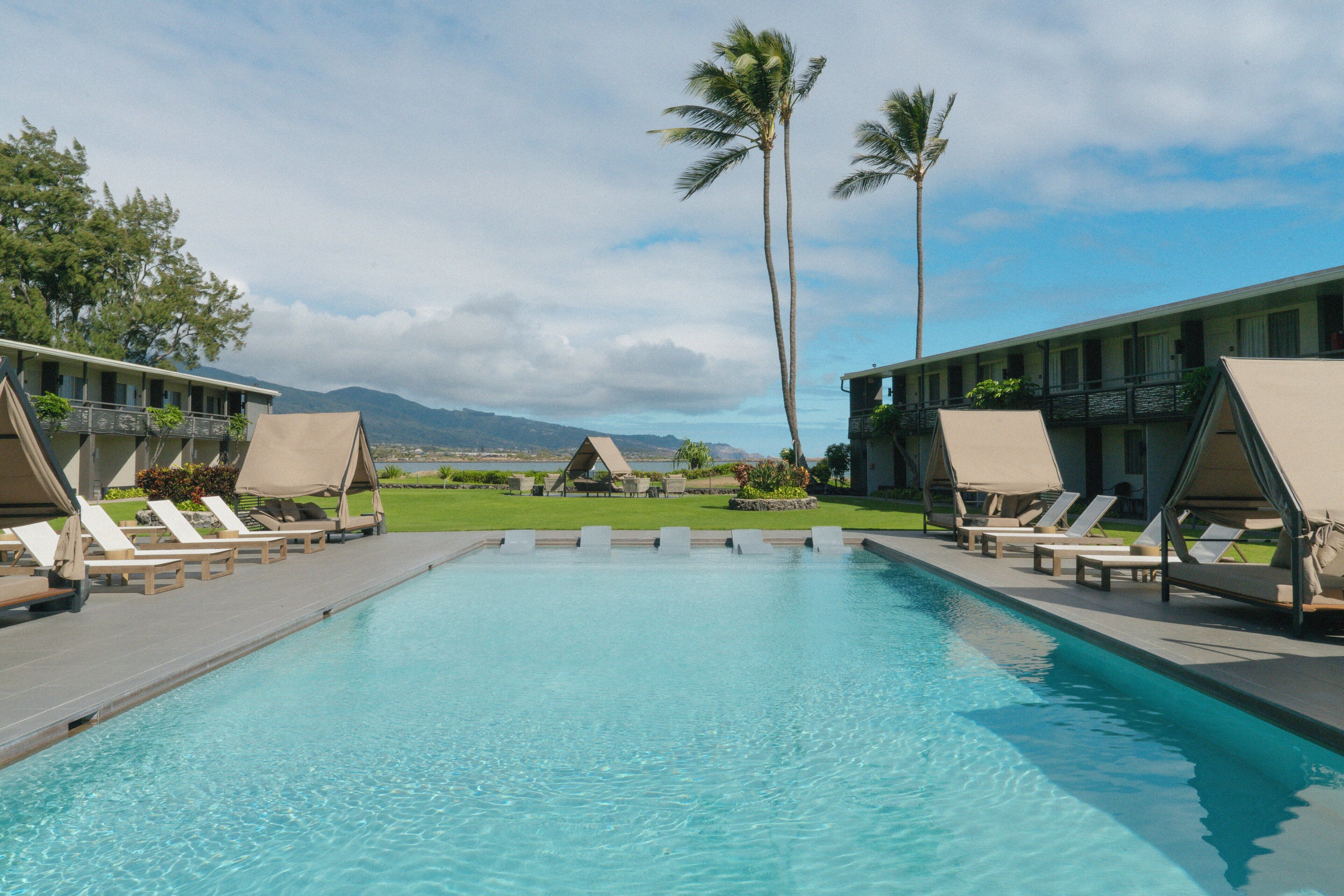 A pool with lounge chairs, a building with balconies, and palm trees.