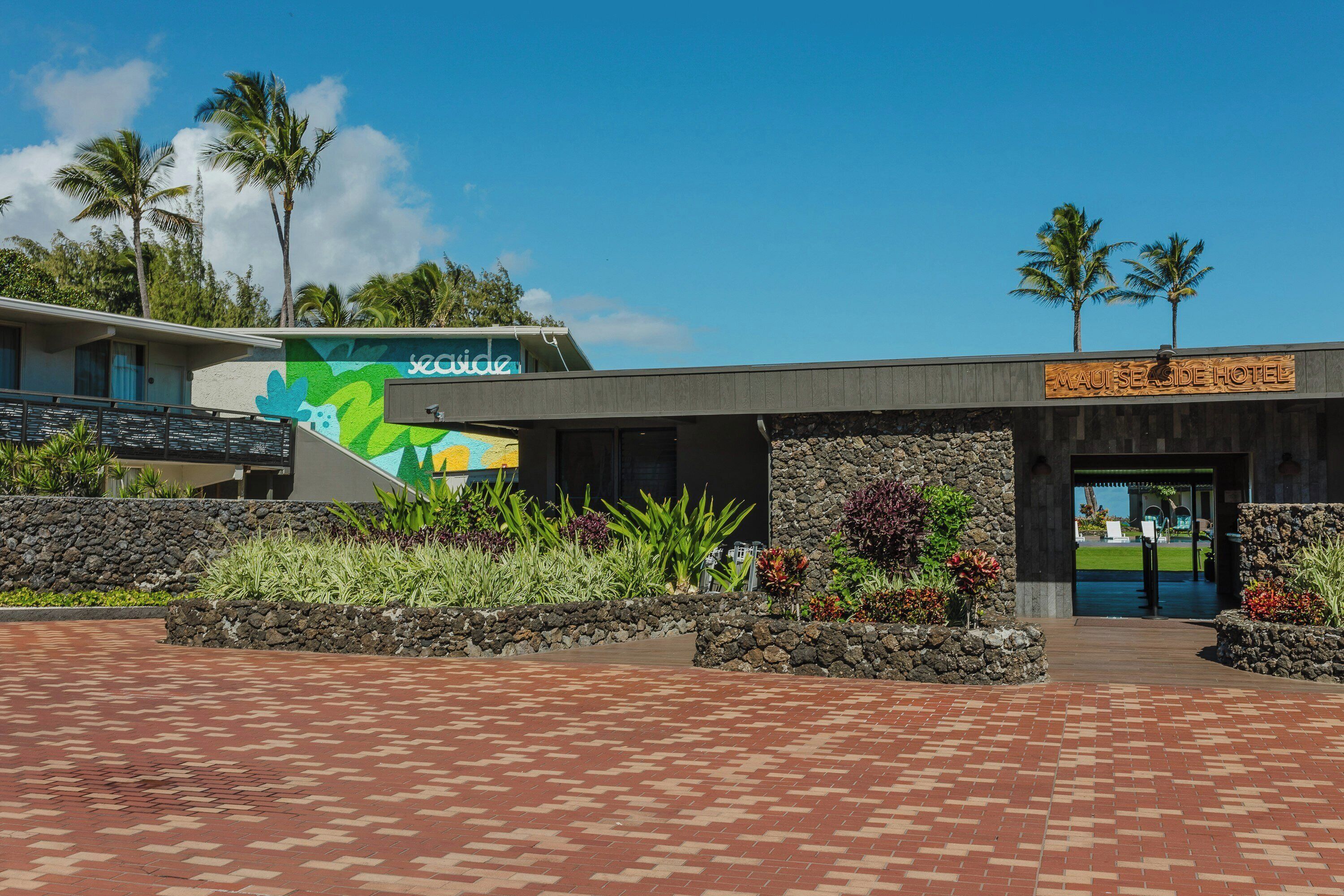 A hotel entrance with a stone facade, a colorful mural, and a clear view of the surrounding greenery.