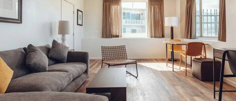 Un salon moderne comprenant un canapé, une table basse, un fauteuil, une lampe et une fenêtre avec des rideaux.