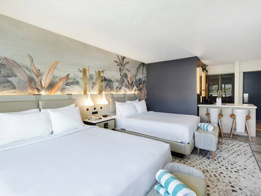 Habitación de hotel con dos camas, un escritorio pequeño y un mural grande en la pared.