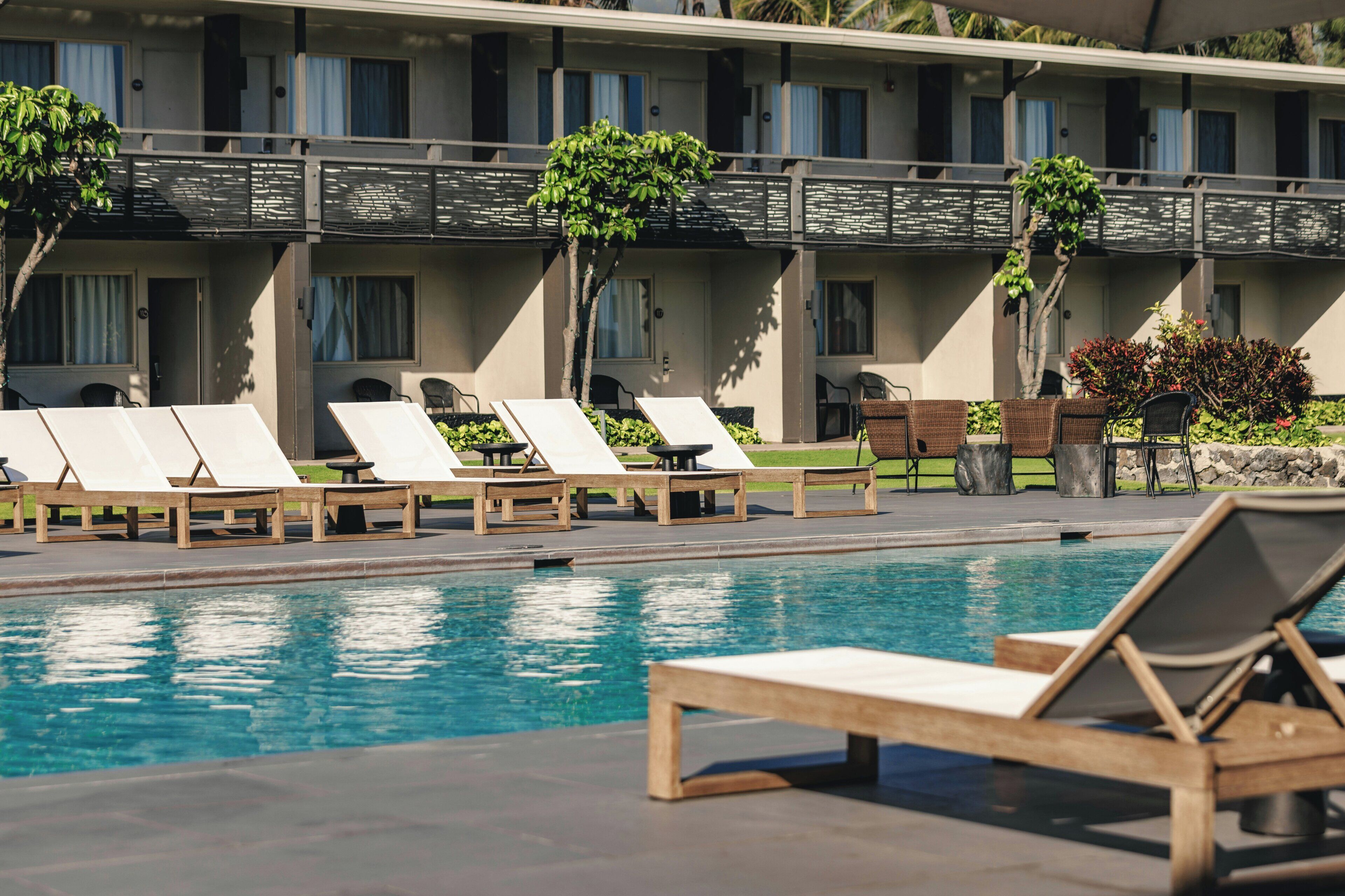 A pool area with lounge chairs and a building with multiple windows and balconies.
